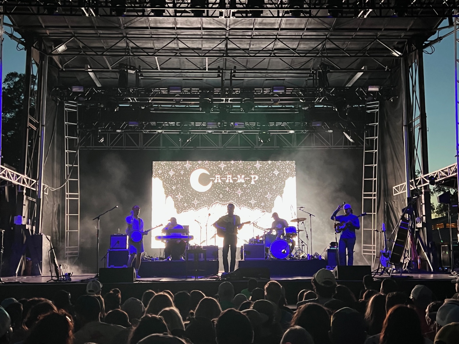 Caamp playing on an outdoor festival stage at dusk